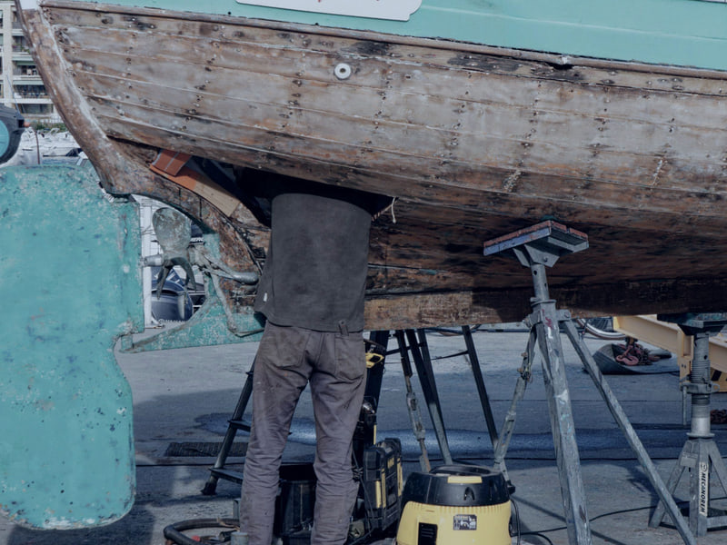 A hull being worked on while the boat sits on stands in a yard