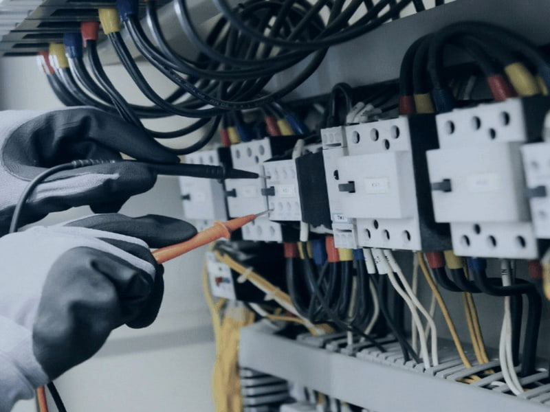 Gloved hands testing terminals in an electrical panel with a probe